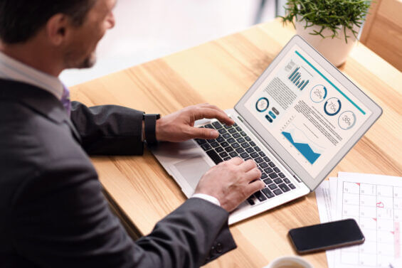 Involved in work. Pleasant senior man sitting at the table and using laptop while working in the office