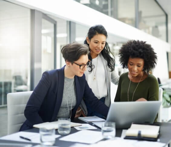 Three business women collaborate at a laptop together.