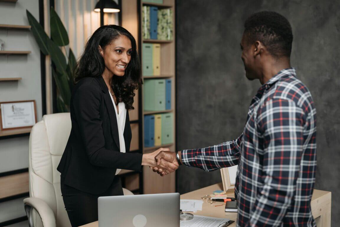 A buinesswoman shakes hands with a client at her desk.