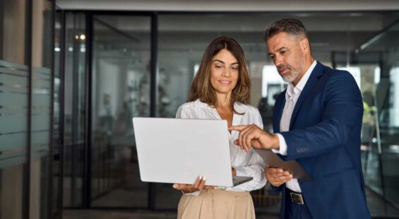 Mature mentor man and European leader woman discussing project on laptop in office. Two diverse partners, colleagues, team of confident professional business people work together. Banner, copy space