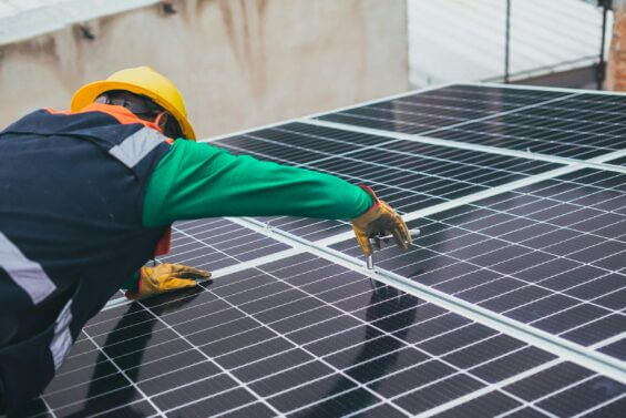 A worker in protective gear performs work on a solar panel.